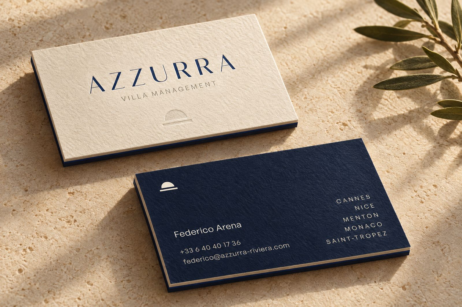 The Azzurra business card, ivory front and night back, on a stone table